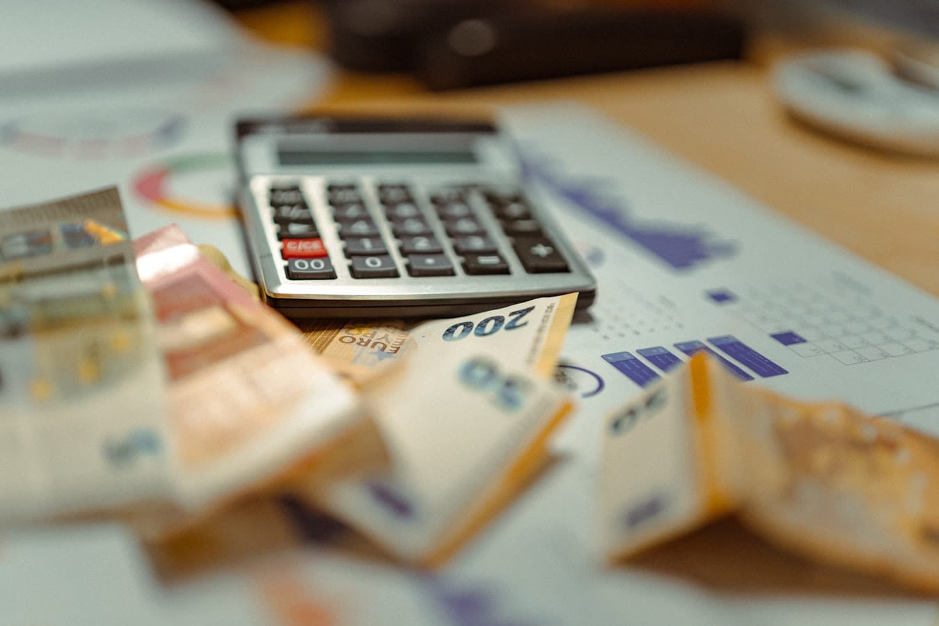 Calculator resting on financial documents with charts and banknotes on a desk