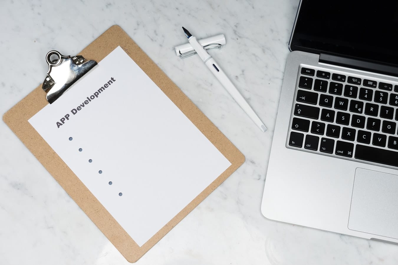 Clipboard holding a planning sheet labeled APP Development beside an open laptop