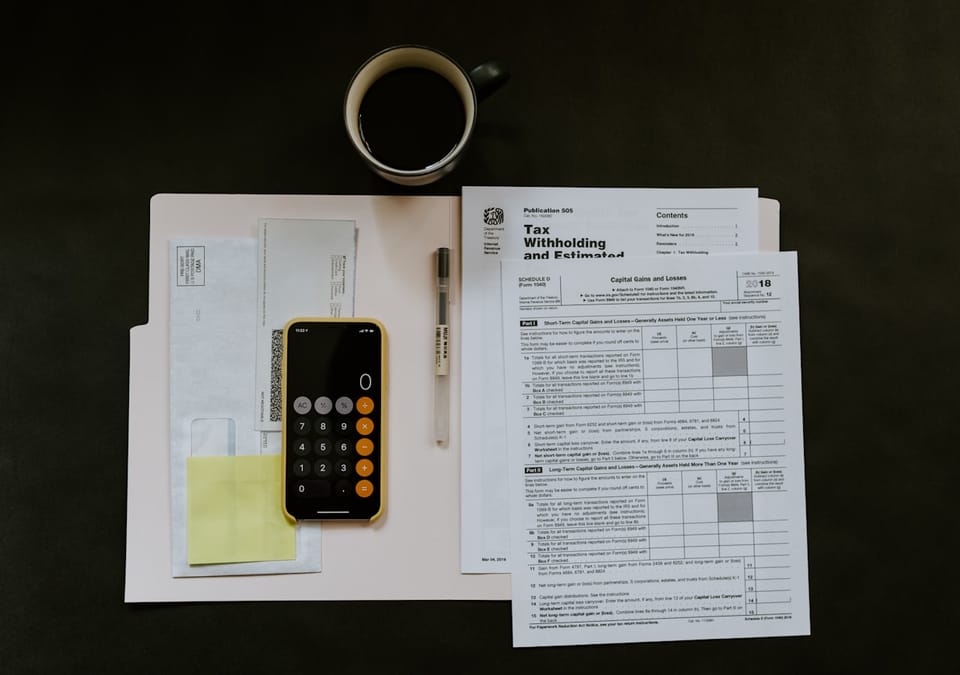Financial documents, tax forms, a calculator app, and coffee laid out on a dark desk