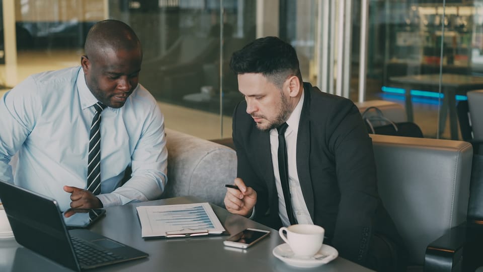 Two businessmen reviewing printed bar charts on a clipboard in a modern office