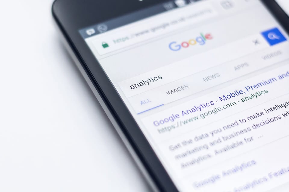 A hand holding a smartphone that displays Google Analytics graphs and website traffic metrics